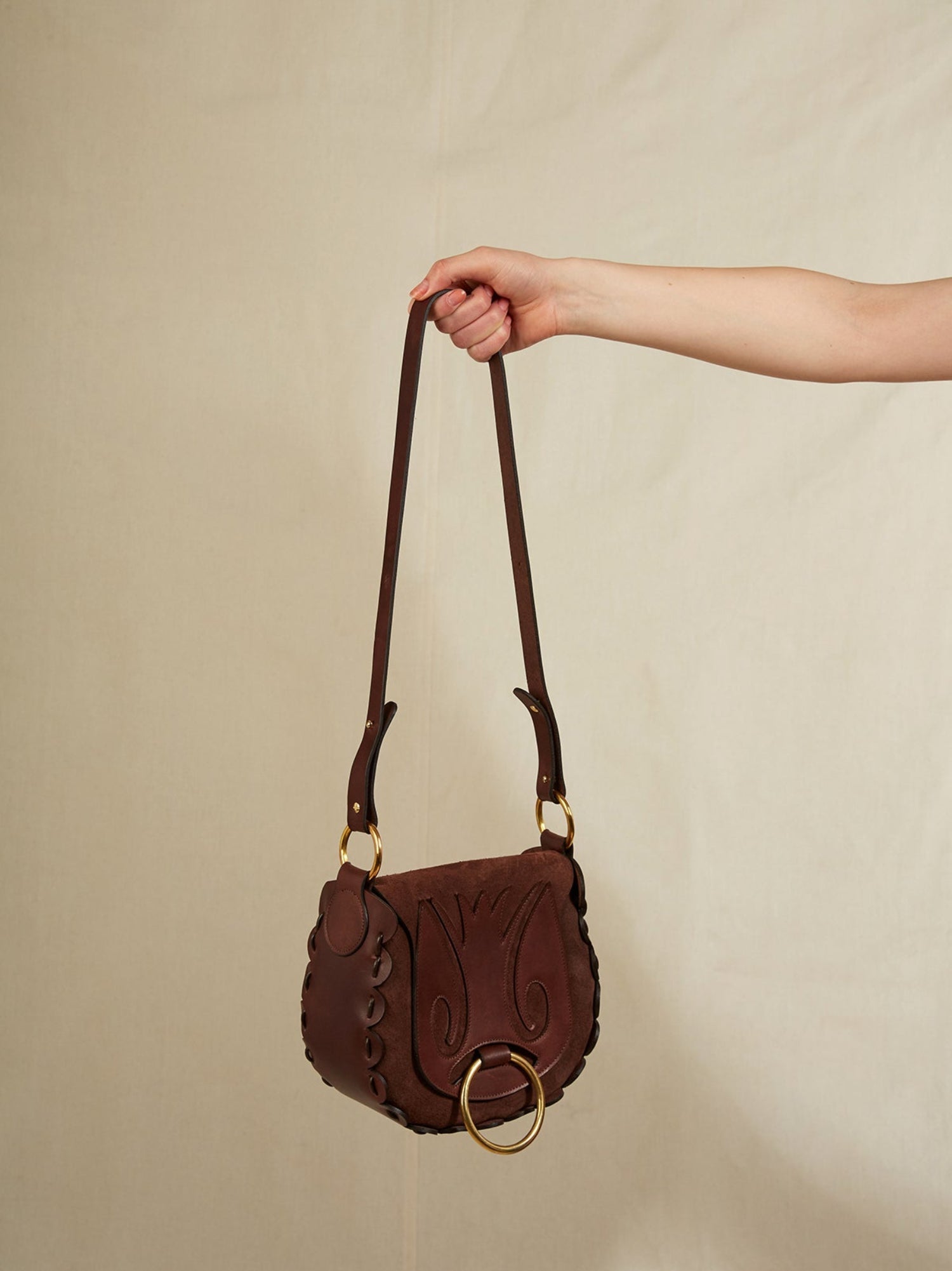 Brown handbag held by a hand against a beige background