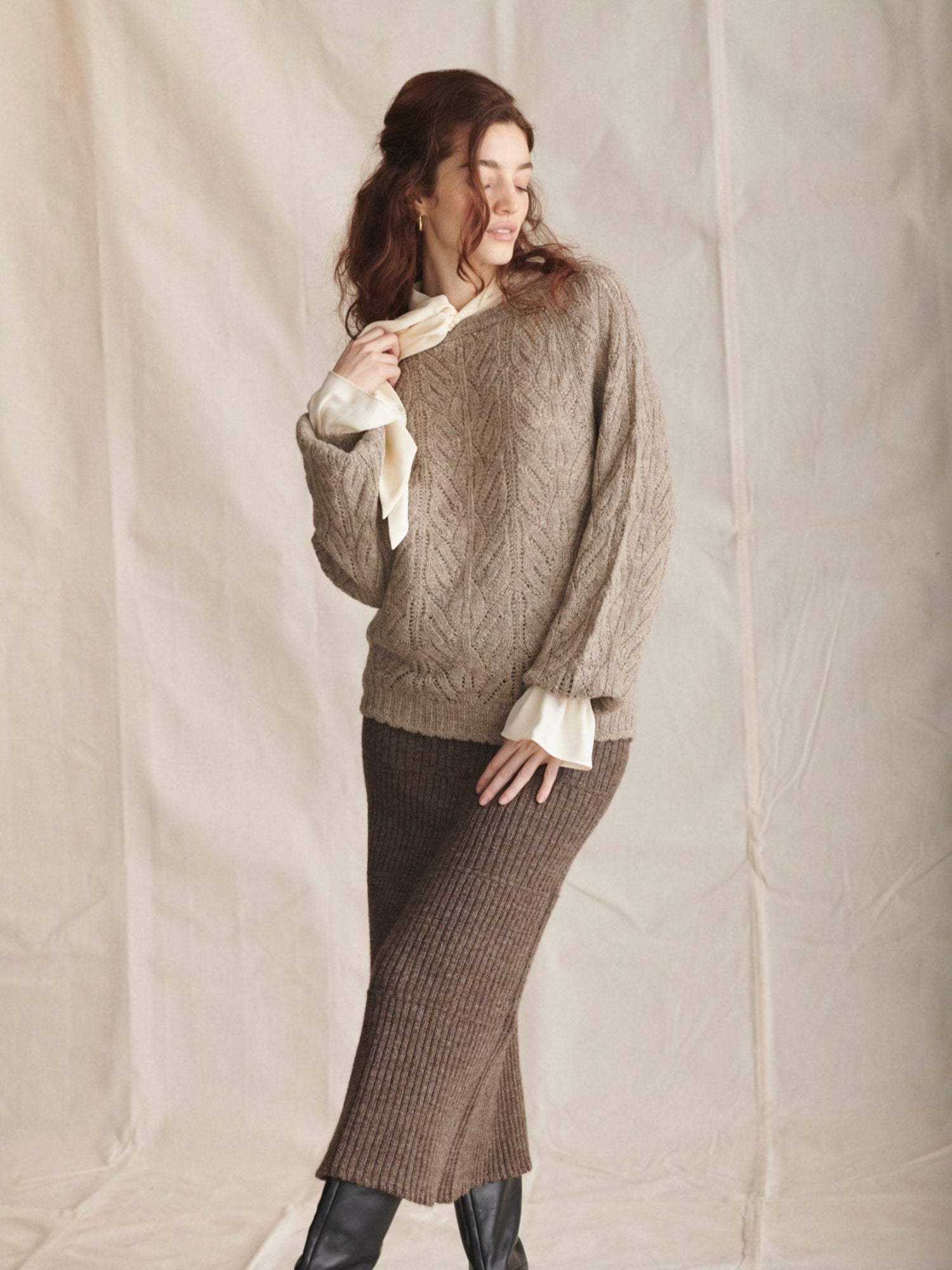 Woman wearing a brown cable knit sweater and matching skirt against a plain background
